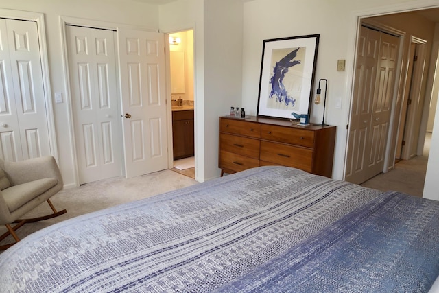 bedroom featuring two closets, light carpet, and ensuite bathroom