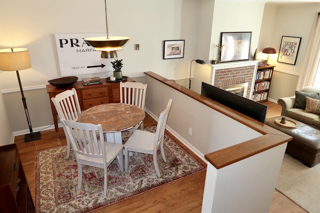 dining room featuring wood finished floors, a brick fireplace, and baseboards