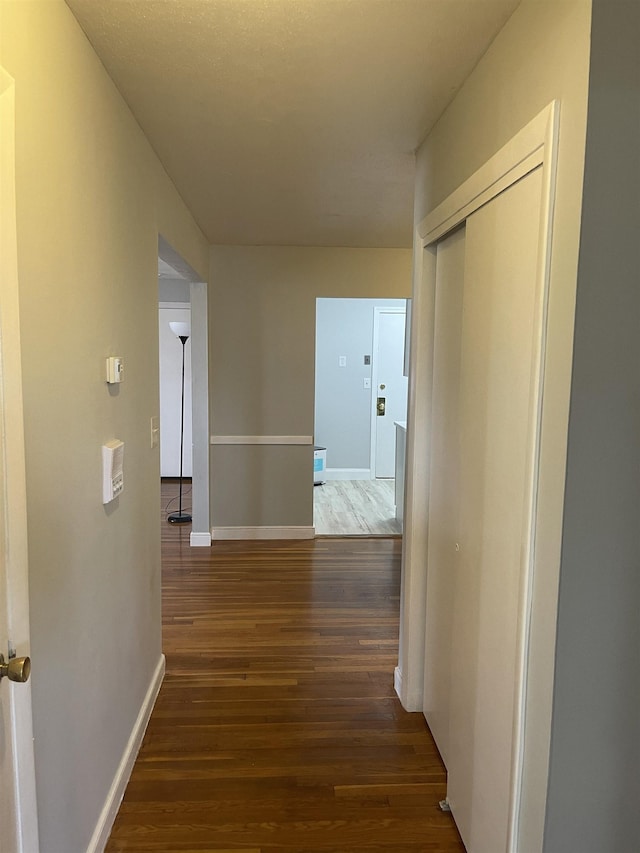 corridor featuring dark wood finished floors and baseboards