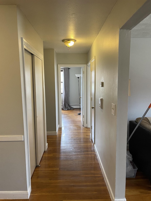 corridor with dark wood finished floors, baseboards, and a textured ceiling