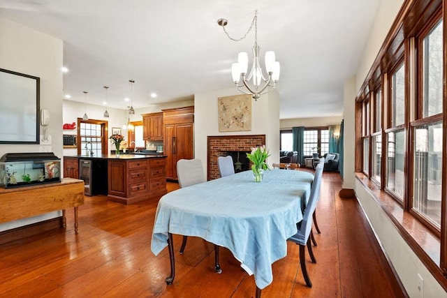 dining area with a fireplace, beverage cooler, a chandelier, dark wood-style flooring, and recessed lighting