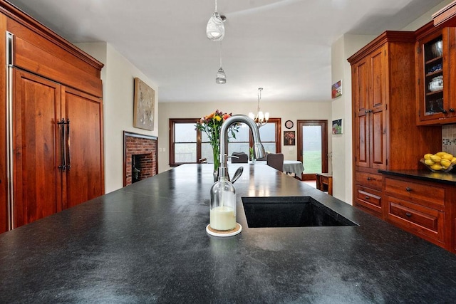 kitchen with a sink, dark countertops, a brick fireplace, pendant lighting, and a chandelier