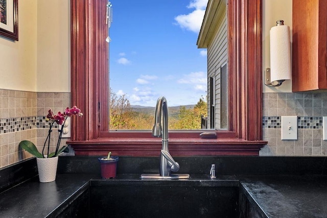 kitchen view of dark countertops, a sink, backsplash, and reddish brown cabinets