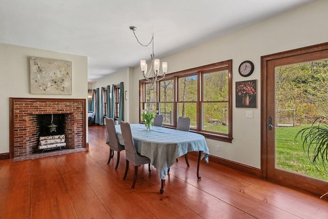 dining space with a chandelier, wood-type flooring, a brick fireplace, and baseboards