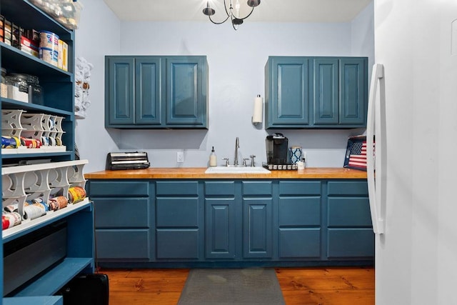 kitchen featuring a sink, blue cabinetry, freestanding refrigerator, and butcher block counters