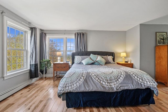 bedroom featuring baseboard heating, multiple windows, wood-type flooring, and baseboards