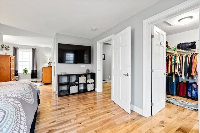 bedroom featuring light wood-style flooring, baseboards, a spacious closet, and a baseboard heating unit