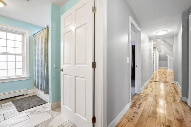 hall with baseboards, a baseboard heating unit, and light wood-style flooring