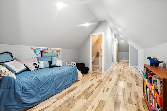 bedroom with light wood-style floors, vaulted ceiling, and ensuite bathroom