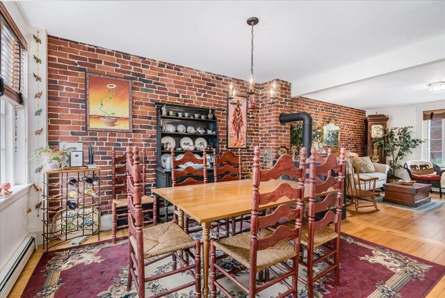 67 Kidder St, Manchester, NH 03101 - dining area featuring baseboard heating, wood finished floors, brick wall, beamed ceiling, and a wood stove