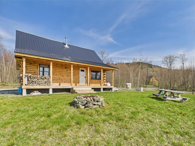 rear view of property featuring metal roof, an outdoor fire pit, log siding, and a yard