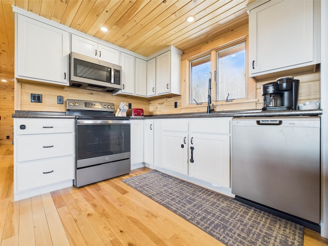 kitchen featuring appliances with stainless steel finishes, wooden ceiling, dark countertops, light wood-style flooring, and white cabinetry