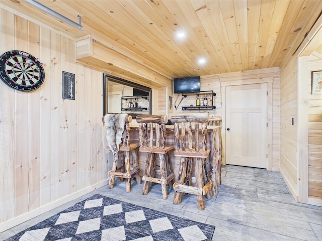 indoor dry bar with wooden walls, wooden ceiling, wood finished floors, recessed lighting, and baseboards