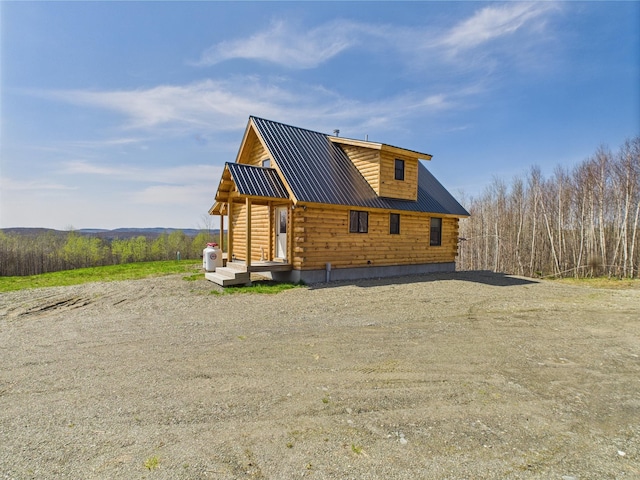 view of side of home featuring log exterior, metal roof, and dirt driveway