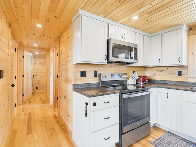 kitchen with stainless steel appliances, wooden ceiling, dark countertops, wood walls, and light wood-type flooring
