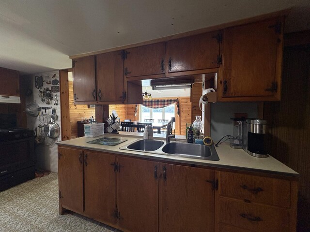 kitchen with a sink, black range with electric cooktop, under cabinet range hood, light countertops, and wood walls