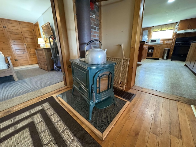 detailed view of a wood stove, white microwave, wood finished floors, stove, and recessed lighting