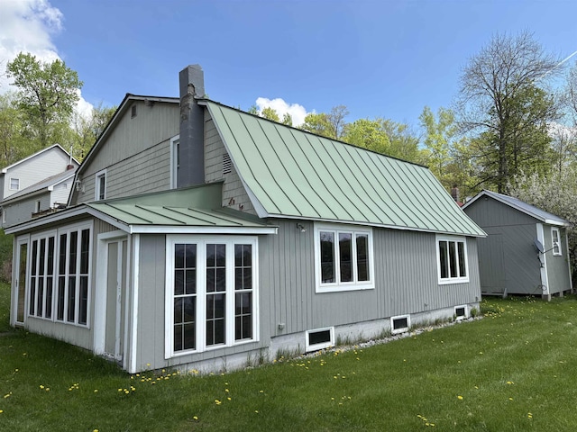 back of house featuring a standing seam roof, metal roof, a chimney, and a yard