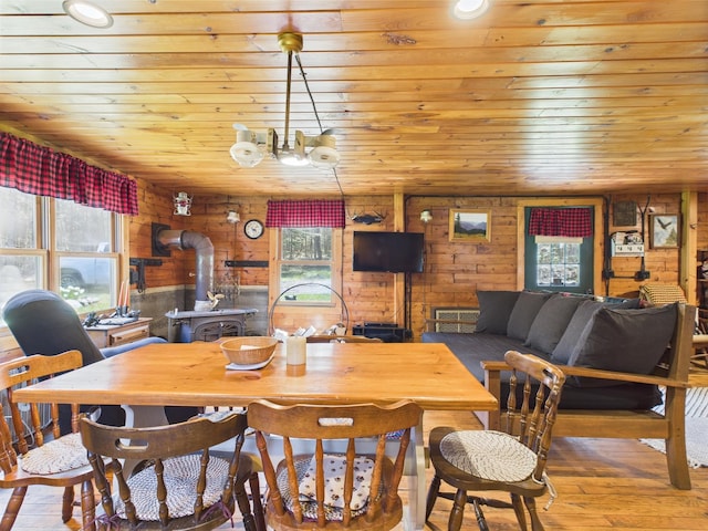 dining room featuring a wood stove, wooden ceiling, wood finished floors, and wooden walls