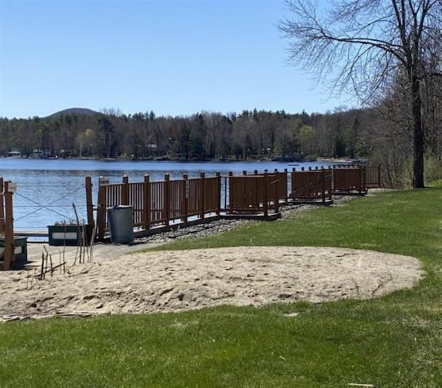 dock area featuring a wooded view, a water view, and a lawn