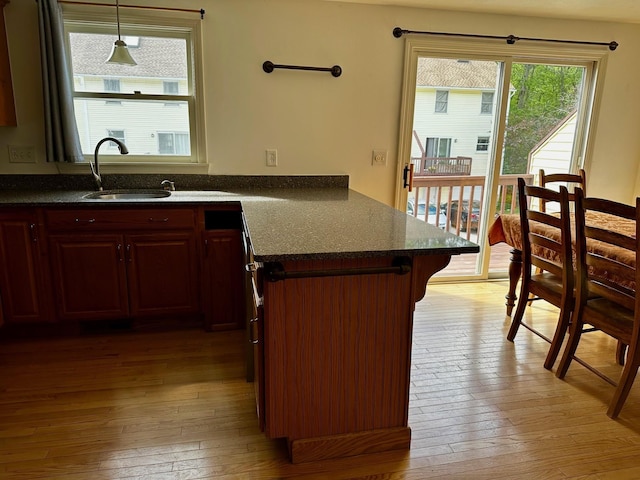 kitchen featuring a sink, light wood-style flooring, a peninsula, and pendant lighting