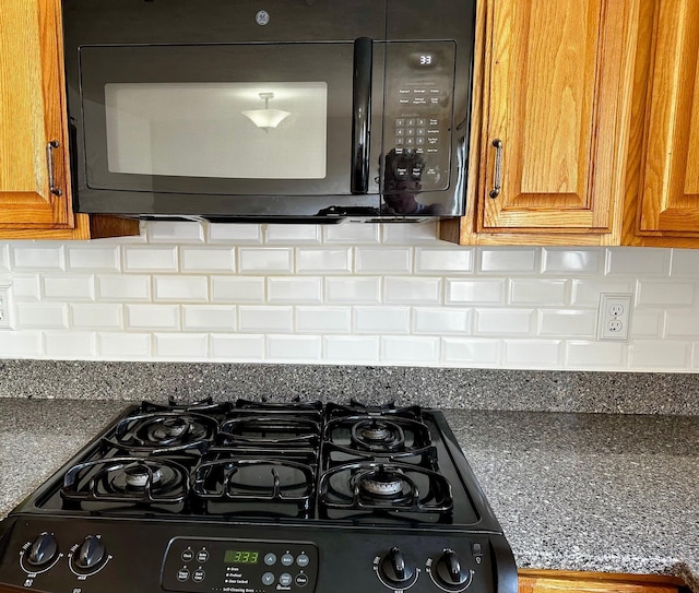 kitchen view of black microwave, gas stove, brown cabinetry, and backsplash