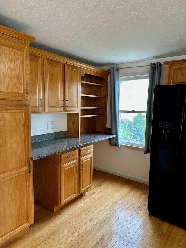 kitchen with black fridge, light wood-type flooring, open shelves, brown cabinetry, and a textured ceiling
