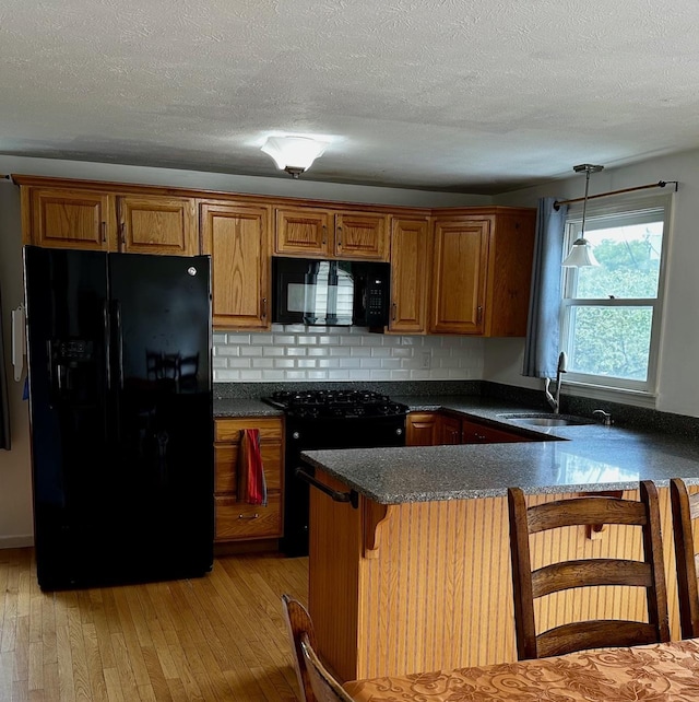 kitchen featuring black appliances, brown cabinetry, a sink, decorative backsplash, and light wood finished floors