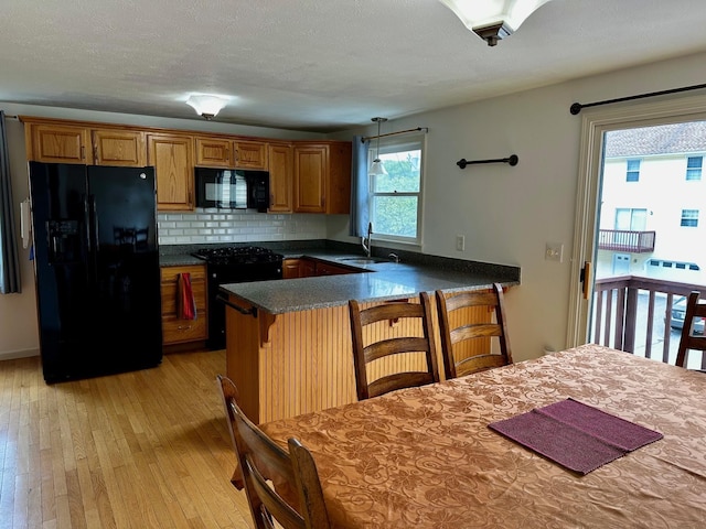 kitchen featuring black appliances, a sink, light wood-style floors, brown cabinets, and a peninsula