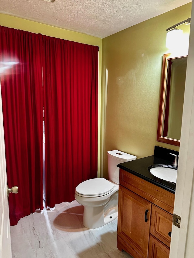 bathroom with a textured ceiling, vanity, and toilet