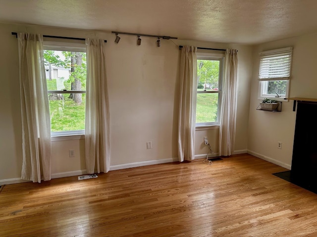 empty room with light wood finished floors, a textured ceiling, and baseboards