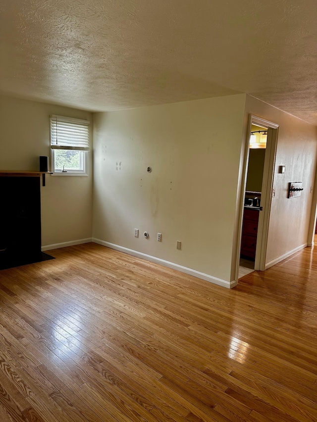 unfurnished living room with a textured ceiling, hardwood / wood-style floors, and baseboards