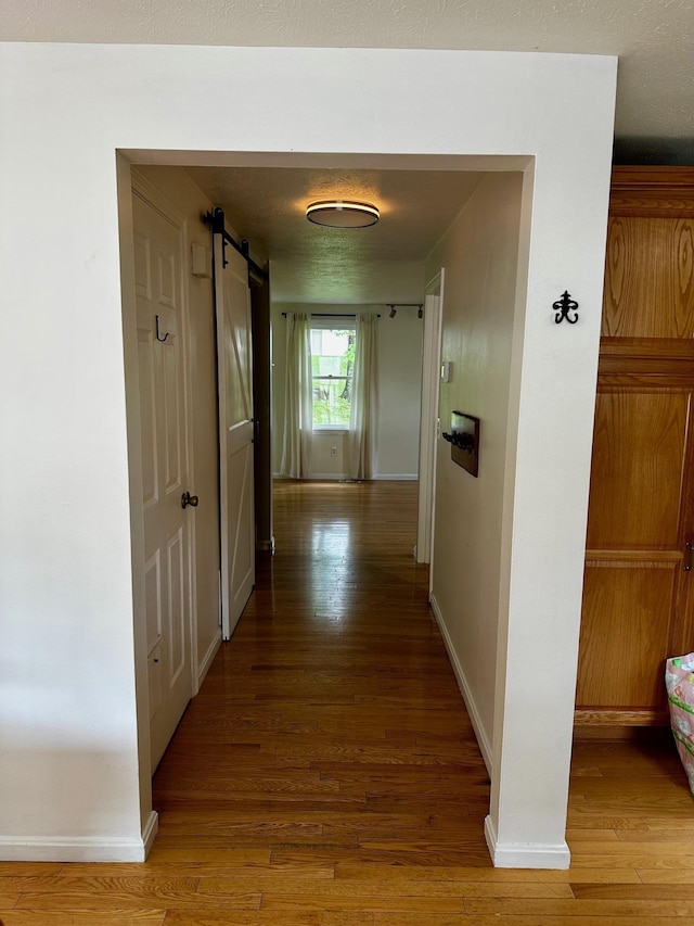 hall featuring wood finished floors, a barn door, and baseboards