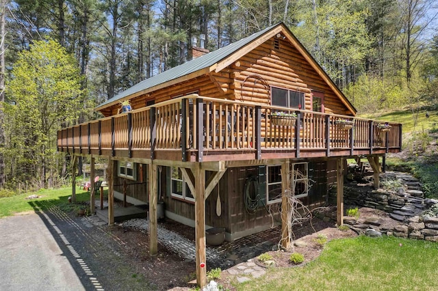 back of property featuring a deck, log siding, metal roof, a chimney, and a forest view