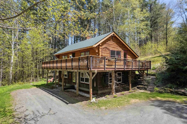 log-style house featuring log siding, a wooden deck, a wooded view, and metal roof