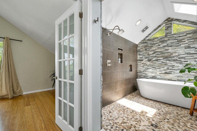 204 Chase Way, Manchester, NH 03104 - bathroom with vaulted ceiling, a skylight, a tile shower, a freestanding tub, and wood finished floors