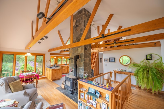 living area with high vaulted ceiling, a wood stove, light wood-style flooring, beamed ceiling, and a ceiling fan