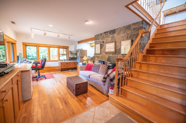 living area featuring stairs, light wood-style floors, a stone fireplace, and a desk