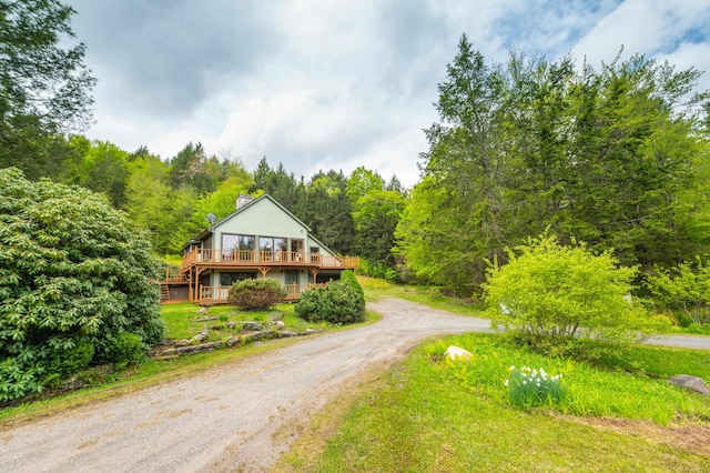 rustic home with driveway, a chimney, a deck, and a view of trees