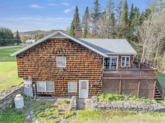 rear view of house with a chimney, roof with shingles, and a deck