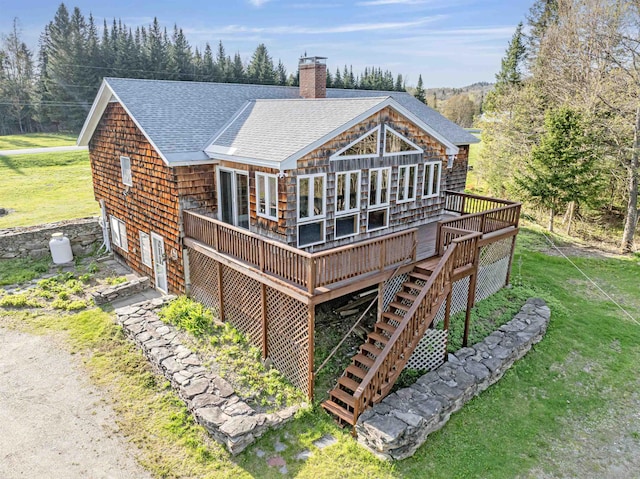 back of house with roof with shingles, a deck, a chimney, and a lawn