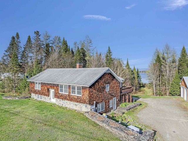 view of side of property featuring a lawn, roof with shingles, a chimney, an outdoor structure, and dirt driveway