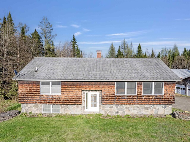 view of front facade with a front yard, a chimney, and roof with shingles