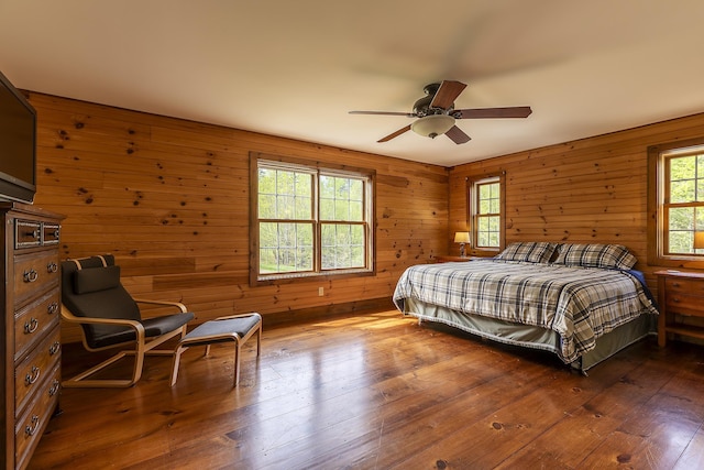 bedroom featuring multiple windows, wooden walls, hardwood / wood-style floors, and a ceiling fan