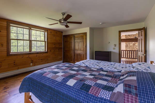 bedroom with wood finished floors, a closet, wood walls, ceiling fan, and baseboard heating