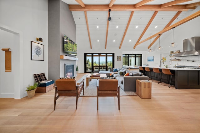 living area featuring high vaulted ceiling, beamed ceiling, a glass covered fireplace, light wood-style floors, and recessed lighting