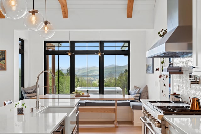 kitchen featuring wall chimney range hood, stainless steel range, beam ceiling, a mountain view, and light countertops