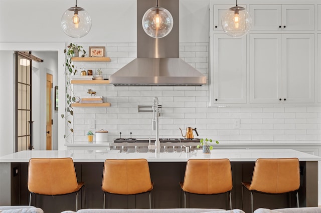 kitchen with wall chimney range hood, light countertops, tasteful backsplash, and a kitchen bar