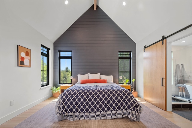 bedroom with high vaulted ceiling, a barn door, light wood-style flooring, baseboards, and wooden walls