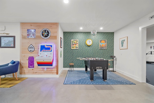 recreation room featuring concrete flooring, baseboards, recessed lighting, and an accent wall